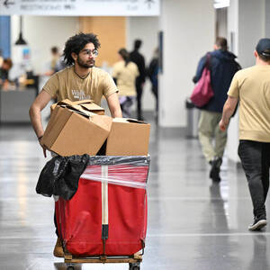 A student pushes a large red cart filled with cardboard boxes