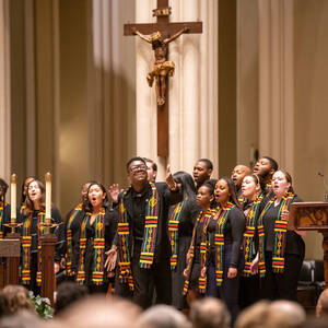 A choir with black robes and green, yellow, red and black scarves, sings