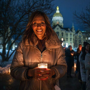 A woman in a winter coat holds a candle outside at night