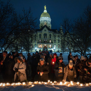 Attendees at a candlelight prayer service place candles. The main building is seen in the background.