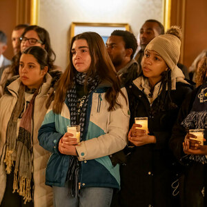 Students in winter coats hold candles as they listen at the candlelight prayer service