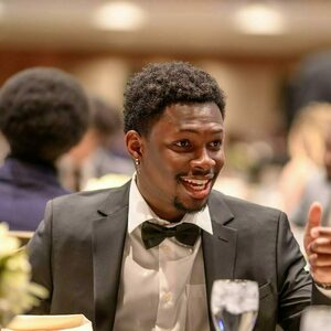 A young black man smiles as he speaks with other people at a dinner table