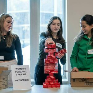 A female student stacks boxes of toothpaste while two other student look on